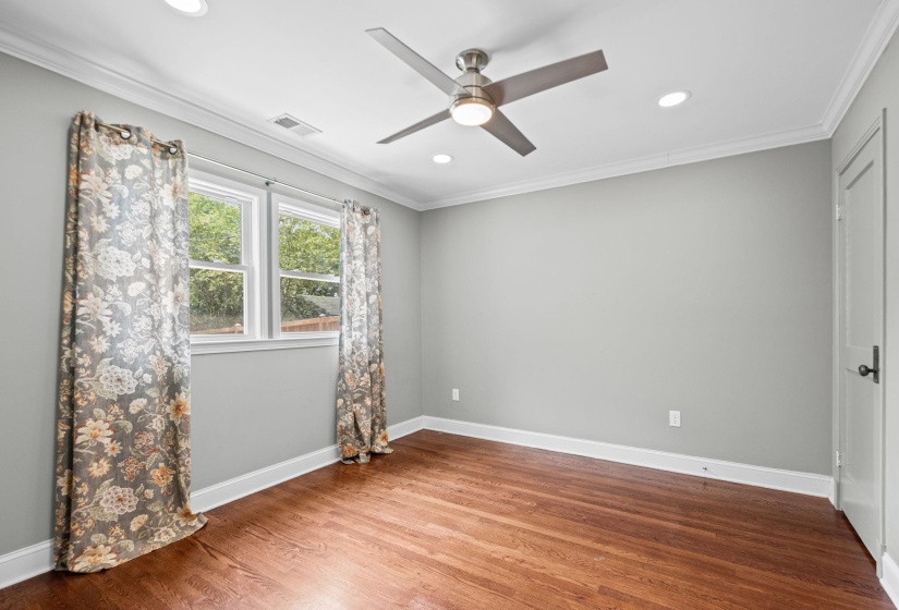 Interior space featuring wood-finish flooring, two large windows, a ceiling fan with integrated lighting, recessed lighting, and crown molding