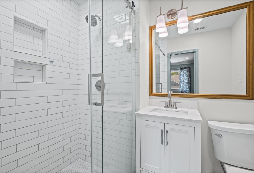 Modern bathroom featuring a glass-enclosed shower with white subway tile, dual shower niches, and a hexagonal tile floor