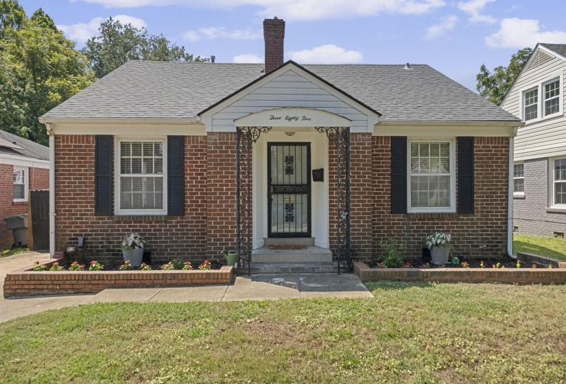 Brick facade home featuring a gabled entryway, black shutters, and a shingled roof