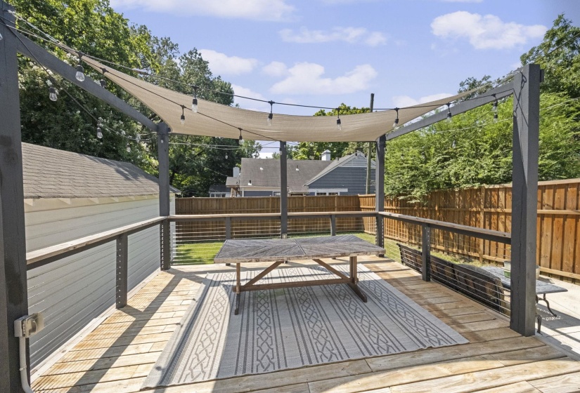 Expansive wood deck featuring a shade sail, string lighting, and cable railing
