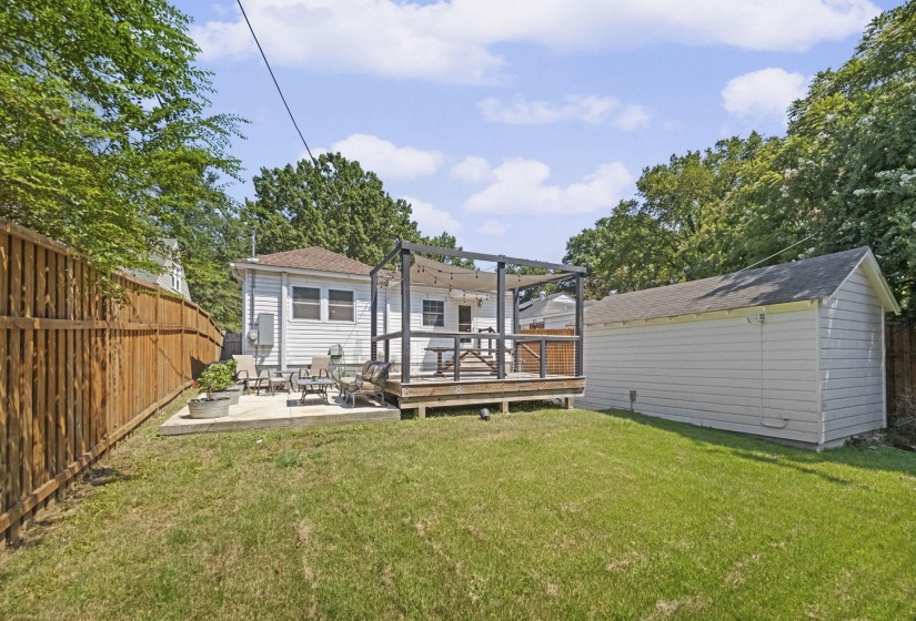 Spacious backyard featuring a wooden deck with a pergola, concrete patio, a detached garage, and a wood privacy fence
