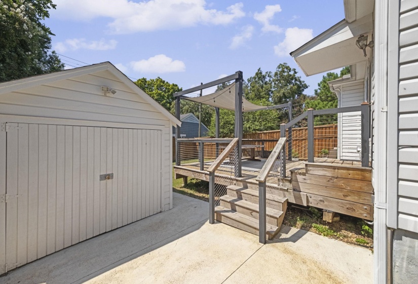 Spacious outdoor deck with modern cable railings and shade sails, complemented by a detached garage with a concrete driveway