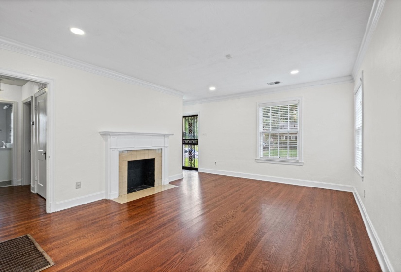 Spacious living area featuring wood-finish flooring, a traditional fireplace with a white mantel and tile surround, recessed lighting, and crown molding