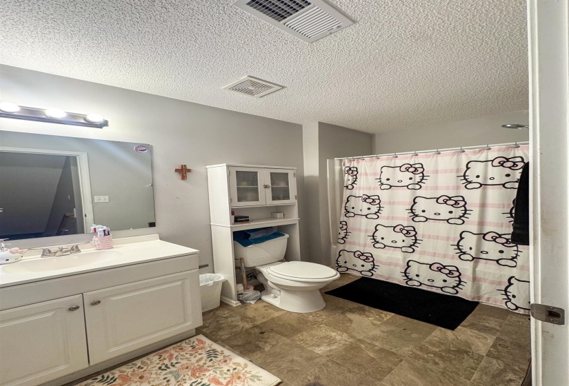 Bathroom featuring a single vanity with a white countertop and cabinet storage, a toilet with an over-the-toilet storage unit, and a shower with a ceiling-mounted showerhead