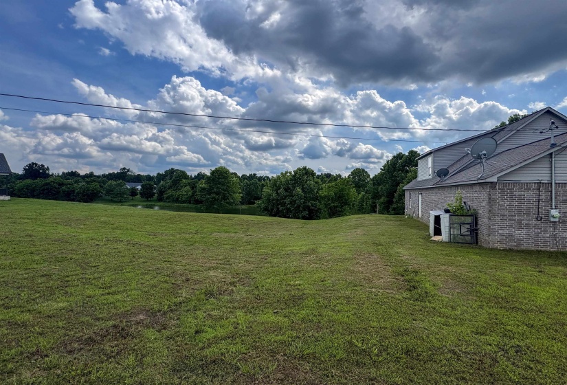 Expansive green space with distant tree line and a tranquil pond feature