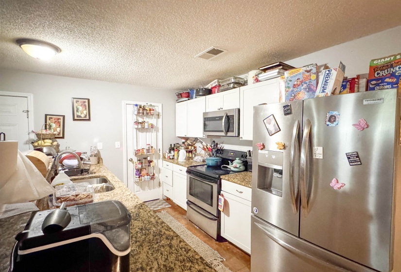 Kitchen featuring granite-style countertops, white cabinetry, a double-basin stainless steel sink, and stainless steel appliances including a refrigerator, range, and built-in microwave