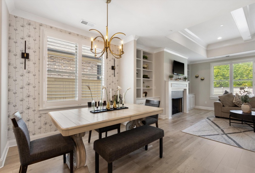 Open-concept living space featuring wood-finish flooring, a decorative fireplace with a substantial mantel, built-in shelving, and a tray ceiling