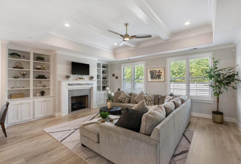 Spacious living area featuring coffered ceilings, wood-finish flooring, a fireplace with a stone surround, and built-in shelving with cabinetry