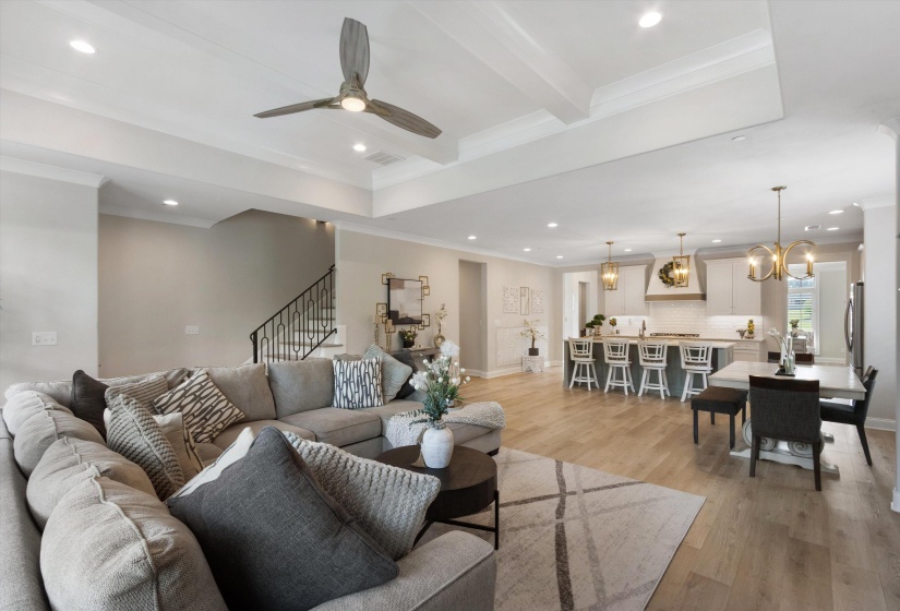 Spacious open-concept living area featuring wood-finish flooring, a tray ceiling with recessed lighting, and a modern ceiling fan