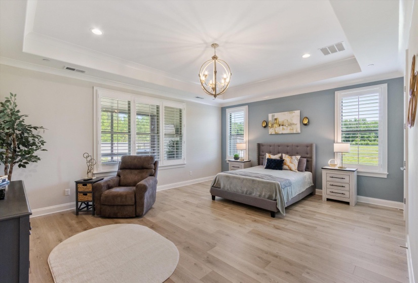 Spacious room featuring wood-finish flooring, a tray ceiling, and a prominent chandelier