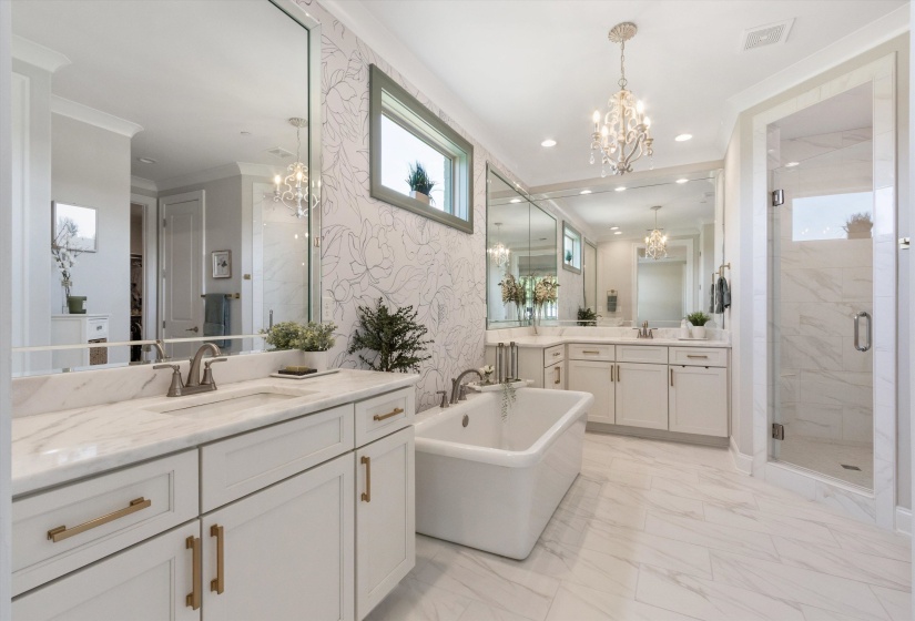 Spacious bath featuring dual vanities with white cabinetry and gold-tone hardware, a freestanding soaking tub, a frameless glass shower, and large format tile flooring
