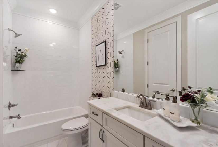 Bathroom featuring a white subway tile tub surround, chrome shower fixtures, a single vanity with a white rectangular undermount sink, a stone-finish countertop, and a large wall-mounted mirror