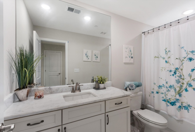 White vanity with a stone countertop, an undermount sink, and a large wall-mounted mirror