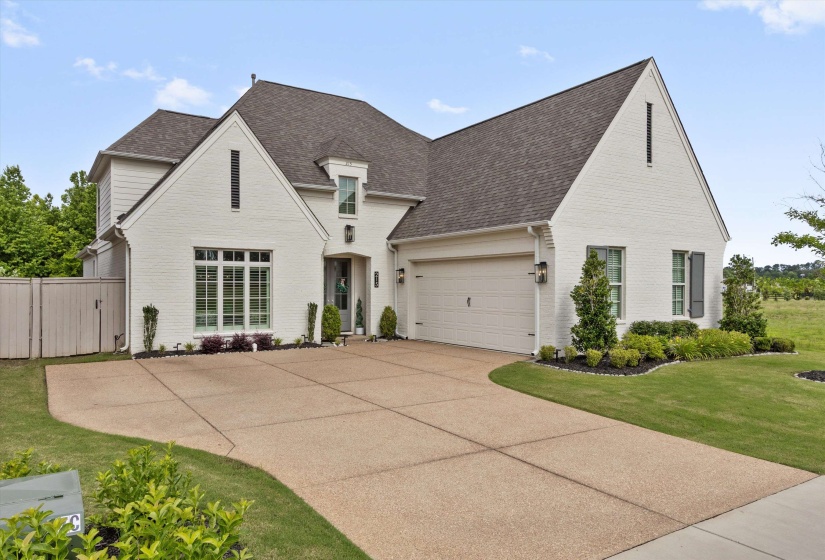 White brick exterior featuring dark shingle roofing, an attached two-car garage, and a concrete aggregate driveway