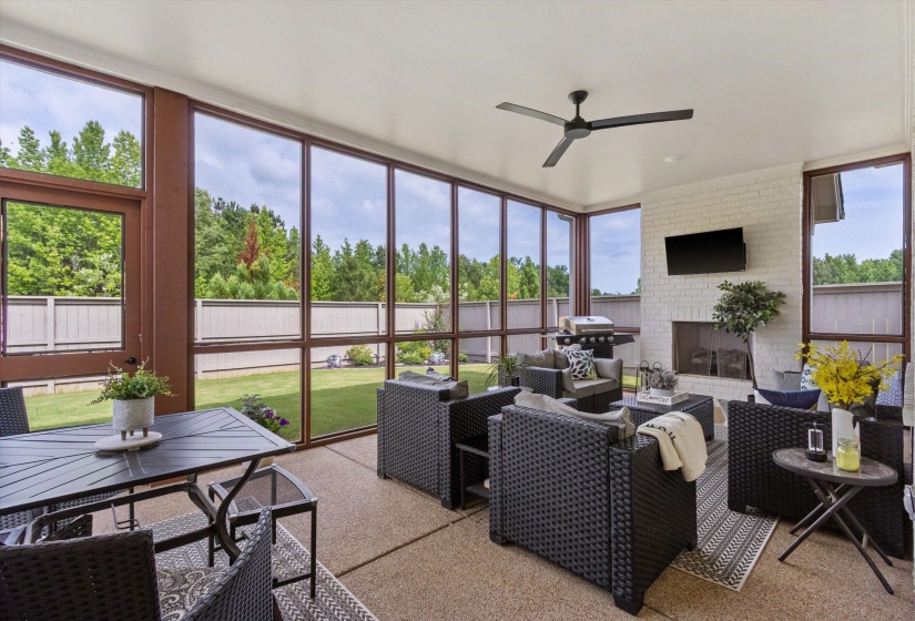 Screened patio featuring a painted brick fireplace, a ceiling fan, a wall-mounted display, and a full-height window wall