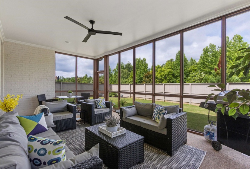 Screened-in porch featuring full-height windows, a ceiling fan, light-colored brick wall, and textured flooring