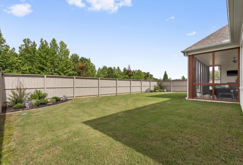Expansive backyard featuring a manicured lawn, full privacy fencing, and a dedicated planting bed