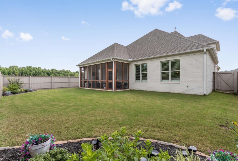 Expansive backyard featuring a screened porch, white brick exterior, private wood fencing, and a manicured lawn