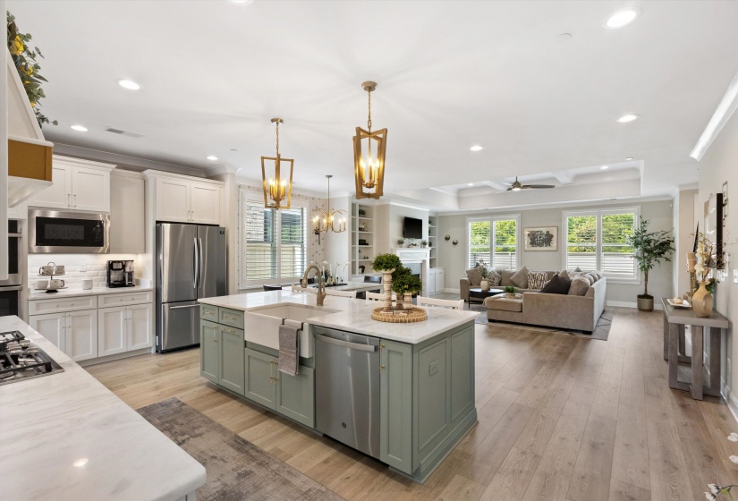 Open-concept interior featuring light wood-finish flooring, a kitchen island with a farmhouse sink, stainless steel appliances, recessed lighting, and a coffered ceiling