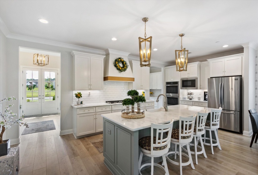 Spacious kitchen featuring a large central island with seating, pendant lighting, stainless steel appliances, white cabinetry, and wood-finish flooring