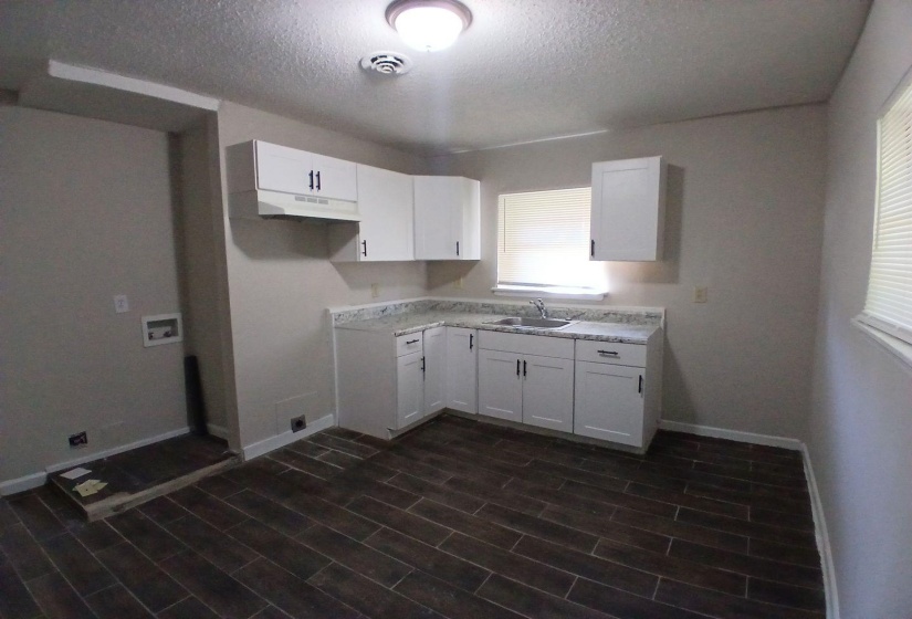 Kitchen featuring white cabinetry with dark hardware, a sink with a window above, and wood-finish flooring