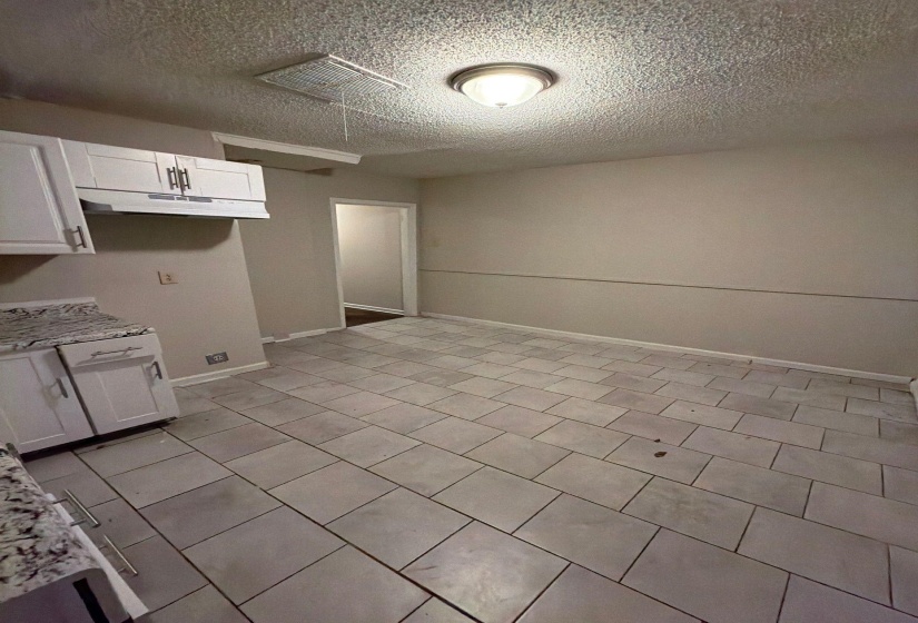 Kitchen area featuring light-toned tile flooring, white shaker-style cabinetry, and granite-look countertops