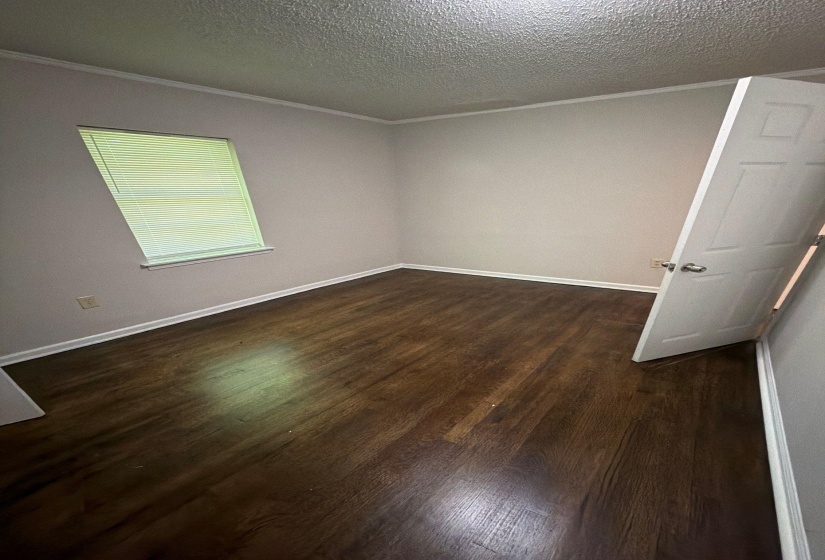 Room featuring wood-finish flooring, a single window with blinds, white baseboards, and a paneled interior door