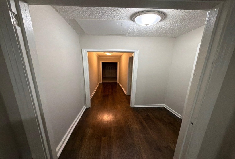 Hallway with wood-finish flooring, light gray wall paint, white baseboards, and overhead flush-mount lighting fixtures