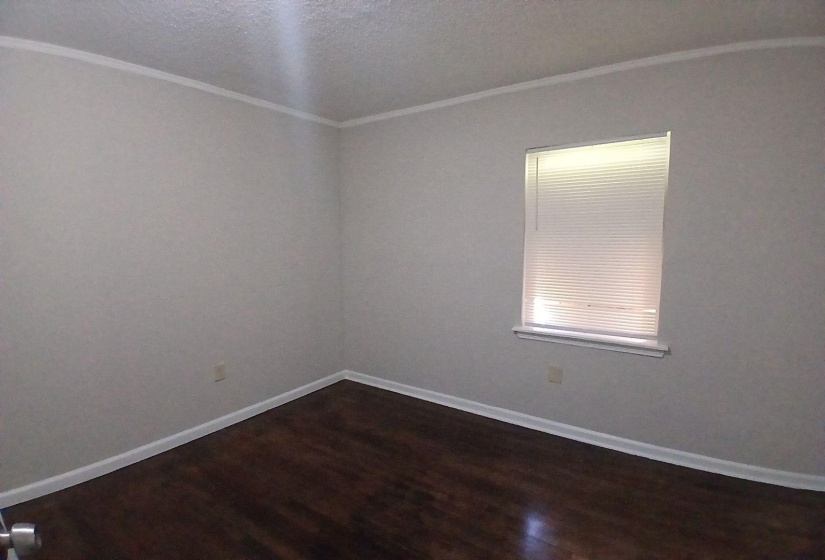 Room featuring wood-finish flooring, light gray walls, white baseboards, and white crown molding