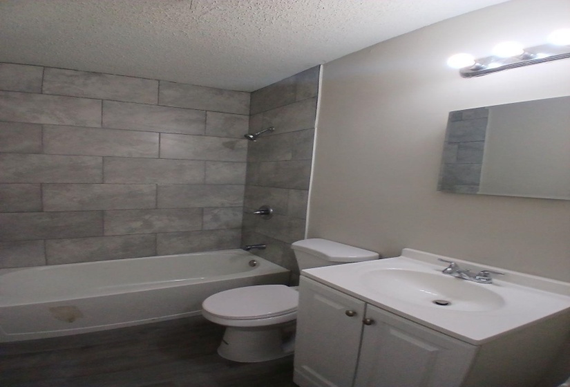 Bathroom featuring a white tub and shower with gray subway tile surround, white toilet, and a white vanity with integrated sink and chrome fixtures