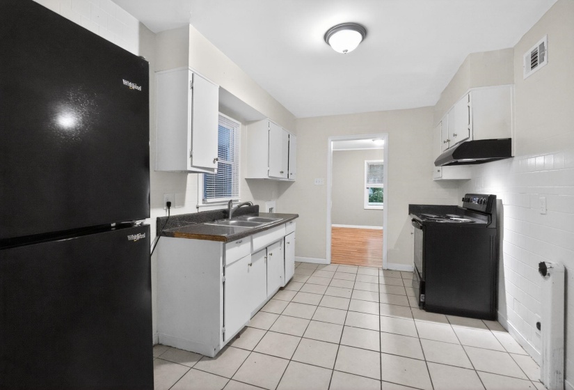 Kitchen with black appliances, white cabinets, dark countertops, and light tile patterned floors