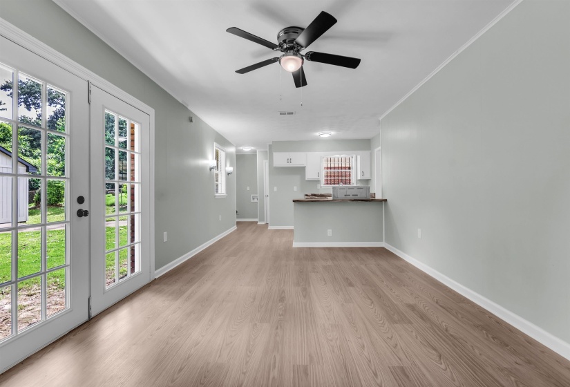 Open-concept living area featuring wood-finish flooring, a ceiling fan with light fixture, and double glass-paned doors leading to the exterior