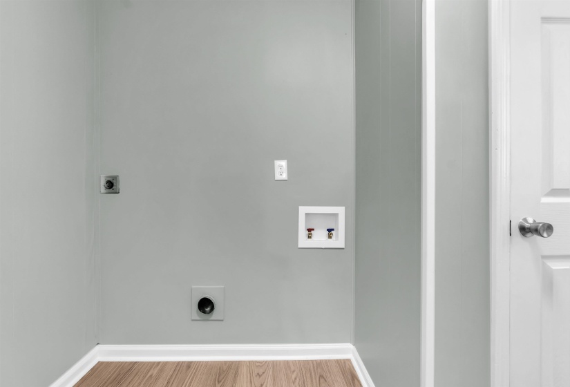 Dedicated laundry area featuring modern hookups, light gray painted walls, crisp white trim, and wood-finish flooring