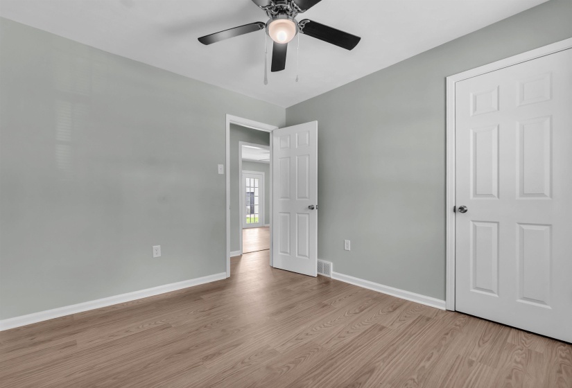 Spacious room featuring light wood-finish flooring, light gray walls, a ceiling fan with integrated lighting, and white six-panel doors