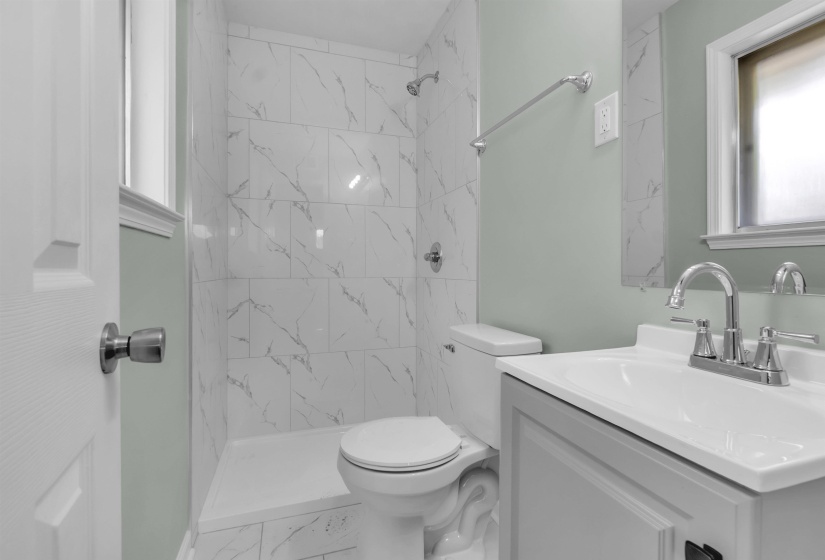 Bathroom with marble-look tiled shower, white toilet, and gray vanity with integrated sink