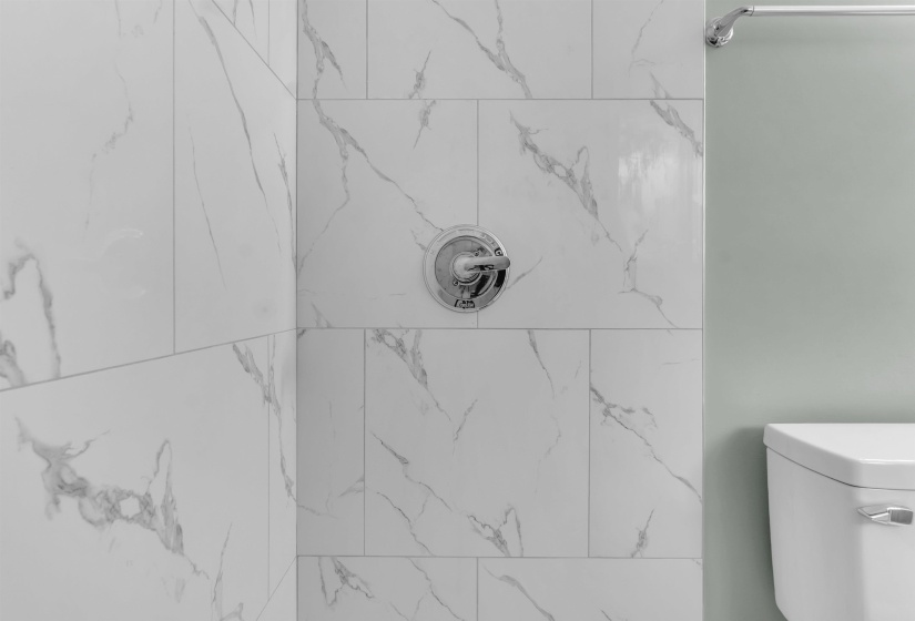 White tiled shower surround with grey veining, chrome shower fixture, and a partial view of a white toilet