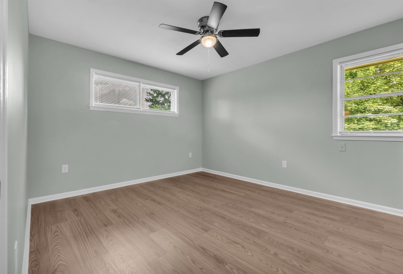 Spacious room featuring wood-finish flooring, two windows with white blinds, and a ceiling fan with integrated lighting