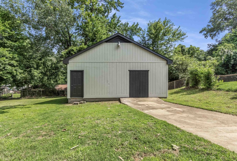 Detached auxiliary structure featuring vertical siding, a dark pitched roof, and a concrete driveway
