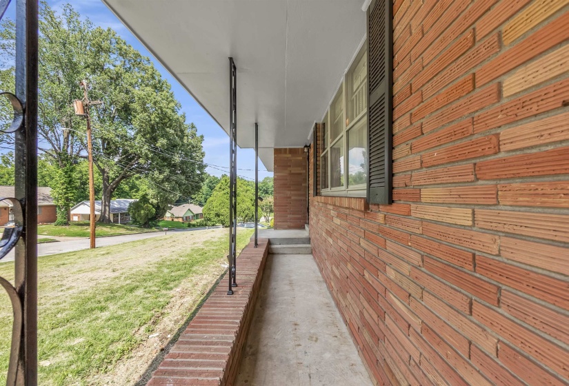Covered concrete porch with decorative wrought iron railing and a brick facade featuring horizontal windows with dark shutters