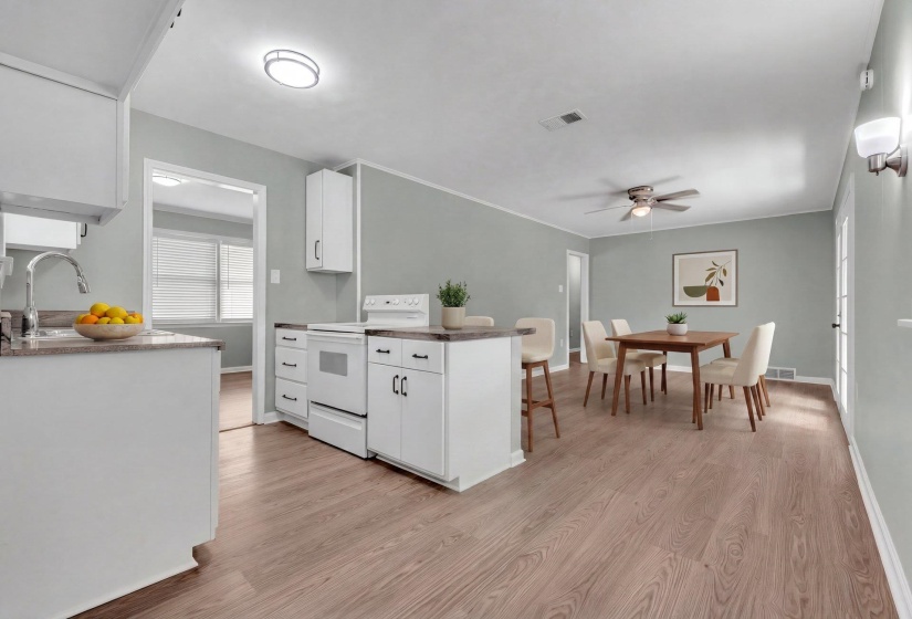 Open-concept living space featuring wood-finish flooring, white cabinetry with dark hardware, a built-in electric range, and ample natural light from the glass-paneled door