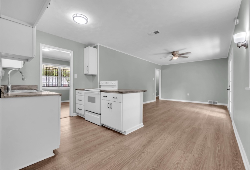 Open-concept living area featuring wood-finish flooring, a ceiling fan with integrated lighting, and a kitchen peninsula with a built-in range