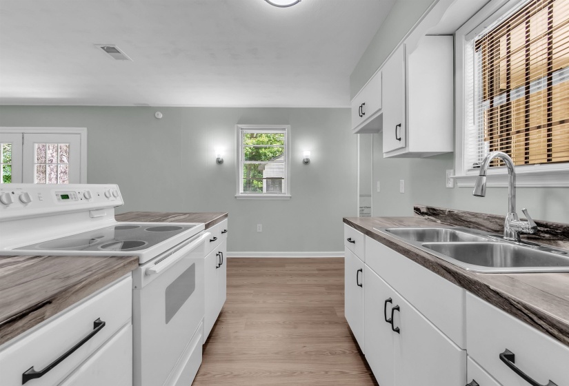 Kitchen featuring white cabinetry with dark hardware, wood-finish countertops, and stainless steel double basin sink with a chrome gooseneck faucet