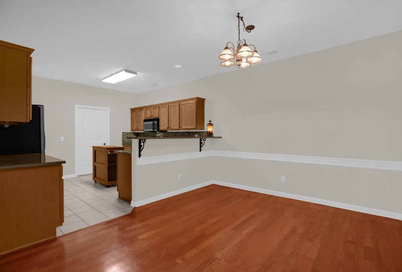 Kitchen and dining area featuring warm wood-finish flooring, a breakfast bar with decorative corbels, and overhead lighting