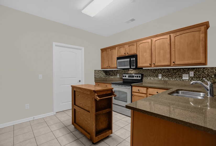 Kitchen featuring light wood cabinetry, stone-look countertops, stainless steel appliances, a mosaic tile backsplash, and tile flooring