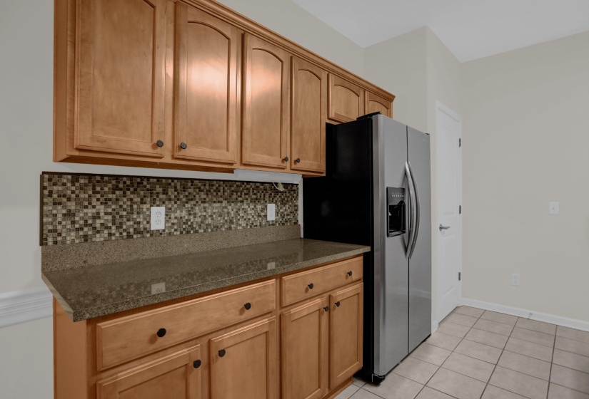 Kitchen featuring wood cabinetry, stone-finish countertops, mosaic tile backsplash, and a stainless steel refrigerator