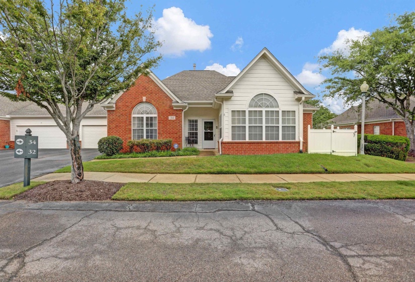 Brick and white siding exterior featuring a prominent arched window, pitched roofline, mature landscaping, and a white privacy fence