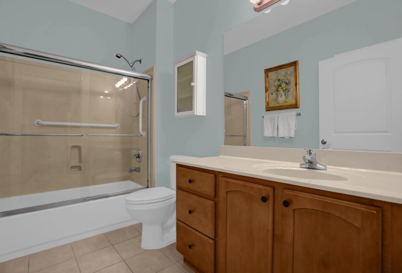 Bathroom featuring a tub and shower combination with sliding glass doors, a vanity with a light-toned countertop, wood-finish cabinetry with dark hardware, a wall-mounted medicine cabinet, and tiled flooring