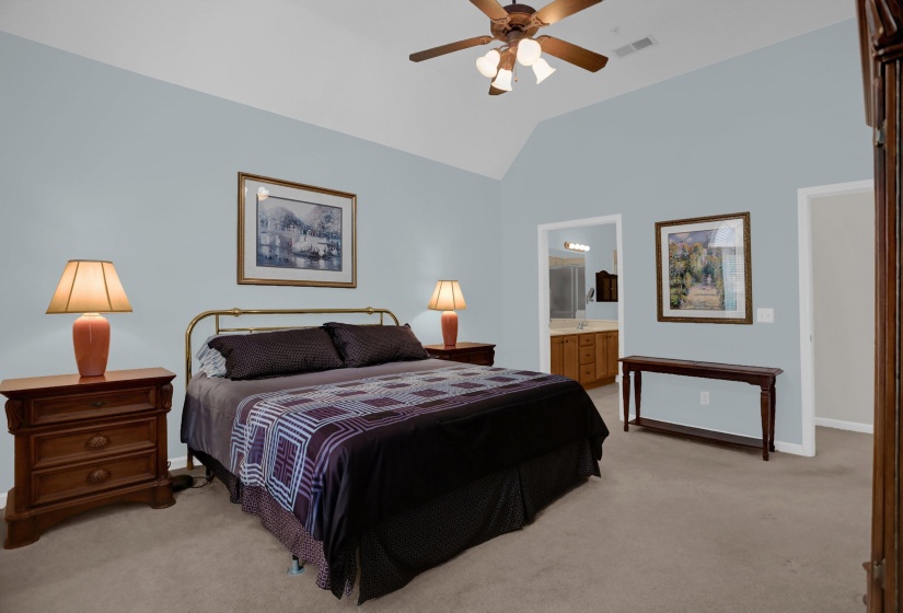 Spacious bedroom with vaulted ceilings, light blue wall paint, and beige carpeting
