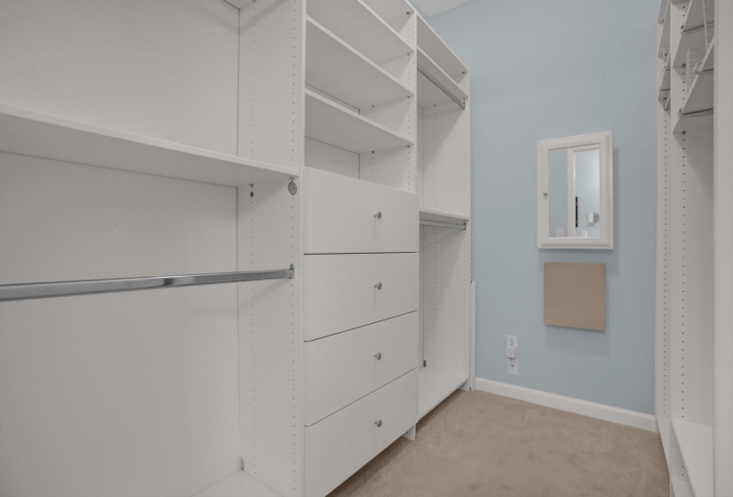 Custom closet system featuring white shelving, multiple hanging rods, and integrated drawer storage with brushed nickel pulls