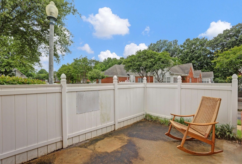 Private patio space featuring a white privacy fence, paved surface, and lush perimeter landscaping